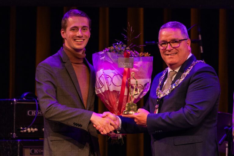 Twee mannen schudden handen met bloemen en trofee.
