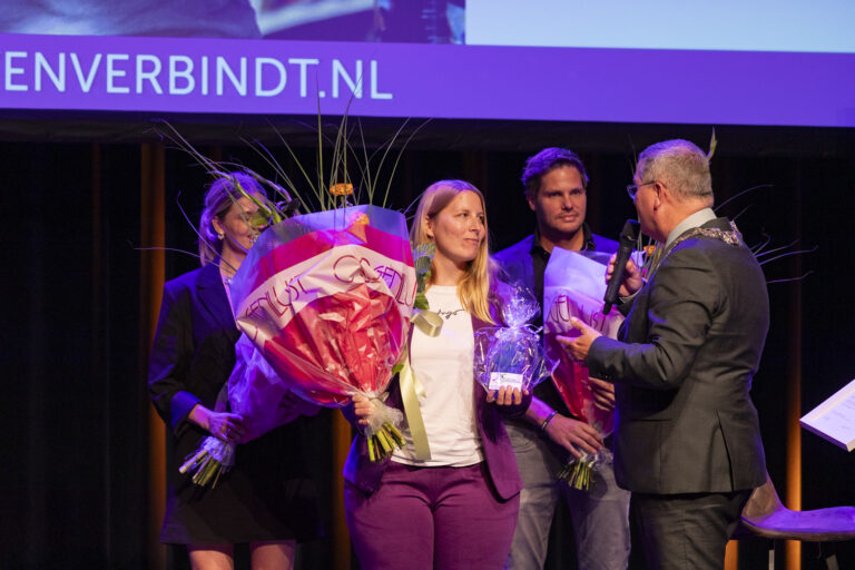 Prijsuitreiking met bloemen en sprekers op podium.