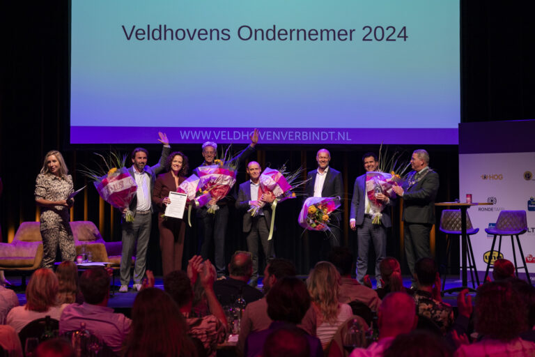 Winnaars Veldhovens Ondernemer 2024 met bloemen op podium.