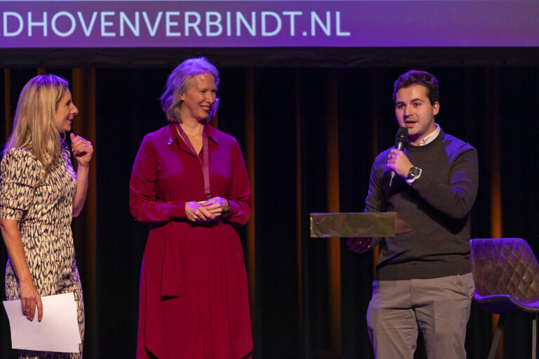 Drie mensen praten op een podium met microfoon.