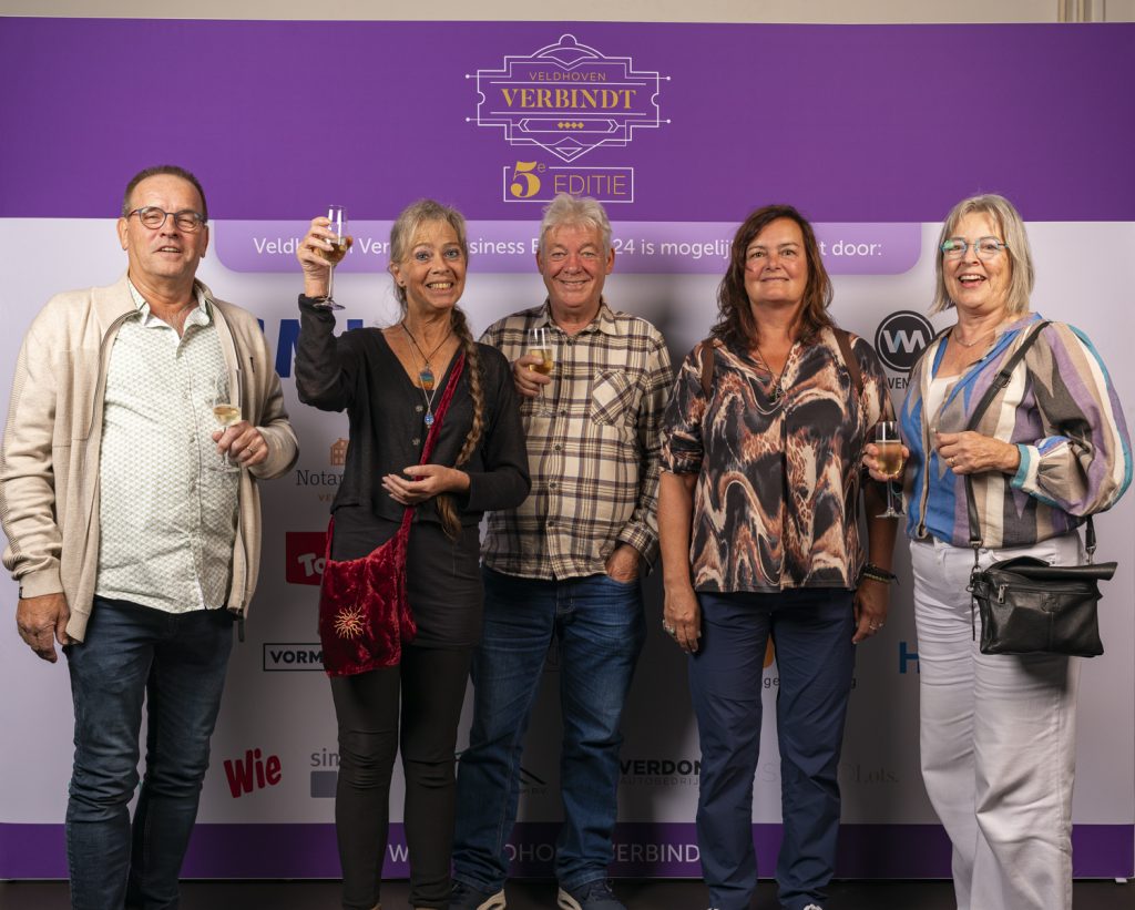 Vijf mensen bij evenementbord met drankjes in handen.