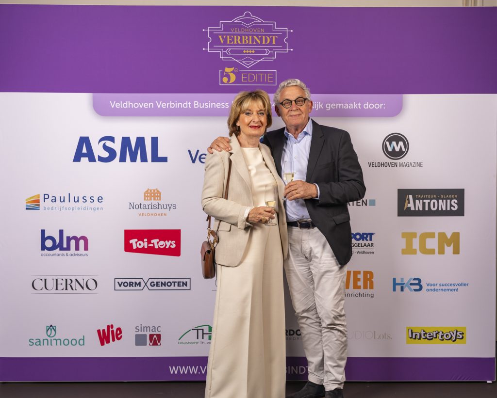 Mensen poseren voor bedrijfslogo's op Veldhoven evenement.