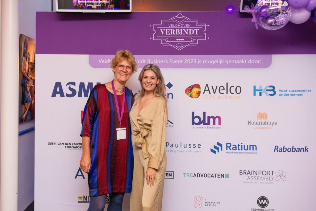 Twee vrouwen poseren voor Veldhoven Verbindt evenement banner.